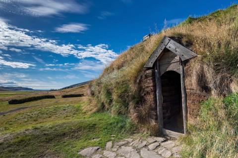 Traditional turf house with wooden door and grass roof in the sunshine, replica of a Viking