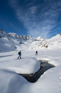 Small stream in a snow-covered mountain landscape, ski tourers in a valley, ascent to the