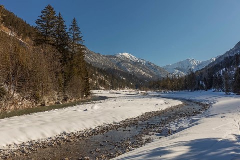 The Riss creek flowing through a snow covered landscape in the Eng valley. Sunny day with blue sky