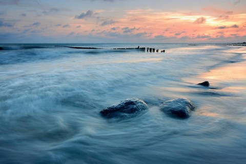 Sunset on the beach, boulders and old groyne in the surf, Klintholm Havn, Møn Island, Denmark,