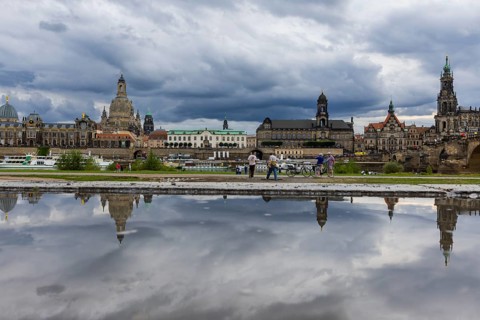 The Dresden silhouette with dark clouds behind the Church of Our Lady is reflected in a puddle on