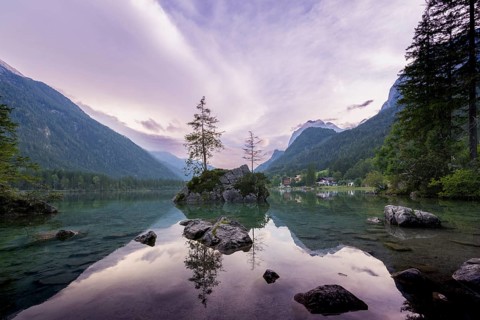Hintersee with rocks and trees in the foreground, surrounded by mountains after sunset with
