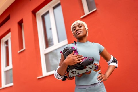 Confident and proud african woman carrying inline skates on shoulders in the city next to house