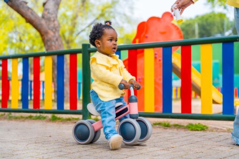 Full length photo of a cute african baby girl riding a toy bike in a park