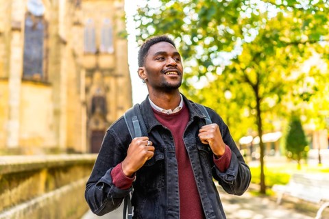 Happy young african man with casual clothes and rucksack enjoying walking in the city