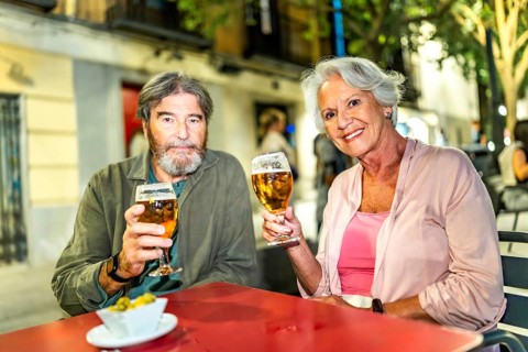 Senior couple toasting at camera with beer in outdoor terrace in the city street