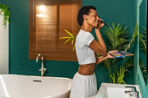 Gay latin man applying make up standing facing bathroom mirror at home