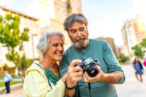 Senior modern caucasian couple looking at the images on a camera screen while visiting a city