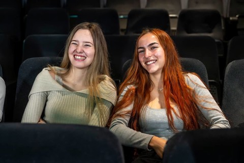 Two happy young women are sitting in comfortable cinema seats, enjoying a movie and smiling