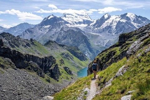 Hiker on hiking trail, mountain lake Lac de Louvie with glaciated summit of the Grand Combin, Val