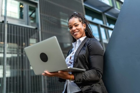 Modern latin businesswoman with long braids working using laptop standing outside a financial