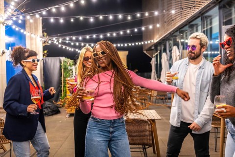 Happy modern african woman with long braided hair dancing with multi-ethnic friends at night party