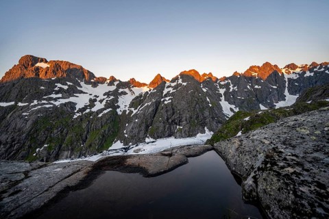 Rocky mountain peaks and Trollfjordvatnet with snow, small pond in moorland at Trollfjord Hytta,
