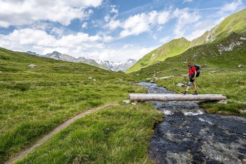 Mountaineer crossing a stream on a tree trunk, mountain landscape with mountain stream, Lasörling