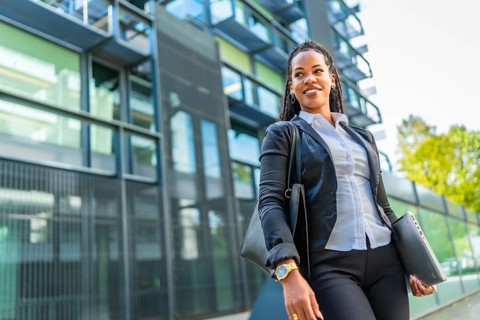 Confident cuban businesswoman walking out the block office carrying handbag and laptop