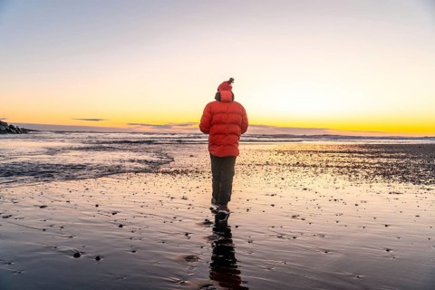 A man in an orange jacket walking at sunrise on Diamond Beach Iceland in winter