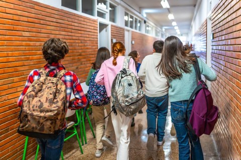 Group of students walking down school hallway between classes, carrying backpacks and rushing to