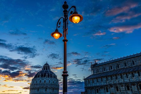 Baptistery and the Cathedral of Santa Maria Assunta at sunset under an illuminated street lamp,