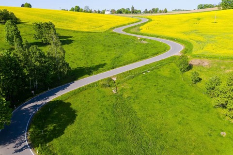 Aerial view of the winding serpentine road between blossoming rapeseed fields from Reifland to