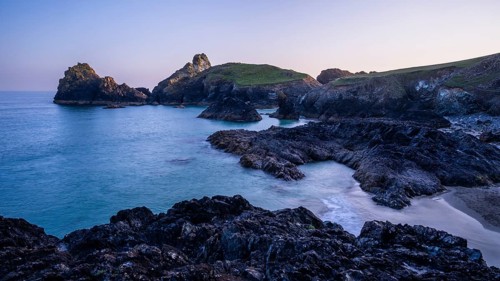 Kynance Cove with Asparagus Island, with sea, sandy beach and rocks in the evening at sunset.