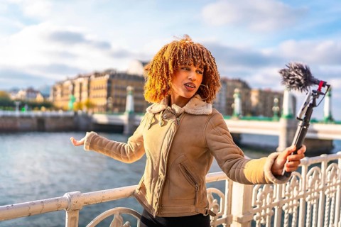 Latin female travel vlogger talking to her audience streaming online next to the river