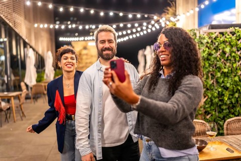 Happy multi-ethnic friends using phone to take a selfie during night outdoor party