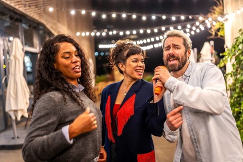 Man singing karaoke with multi-ethnic friends at terrace of bar during night party