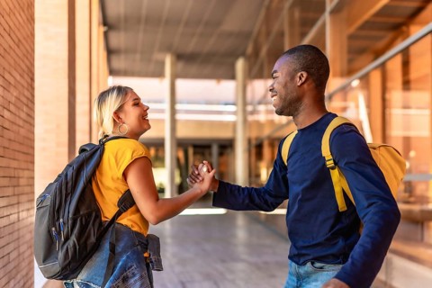 Side view of two happy multi-ethnic students shaking hands at the university