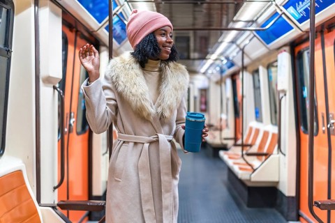 Smiling young black woman wearing winter coat and pink woolen hat holding reusable coffee cup