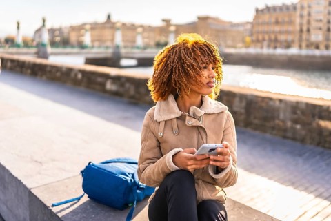 Latin beauty woman using phone sitting in the city next to the river