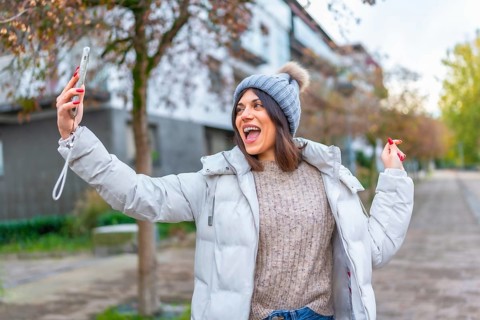 Happy cauacsian young woman smiling during video call with mobile in the street