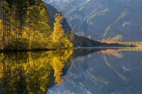 Lake Almsee in autumn with mountains reflected in the lake. Blue sky