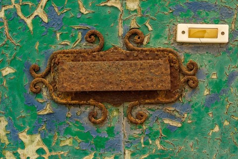 Close-up, old shabby dilapidated front door with antiquated rusty mail slot and yellowed doorbell