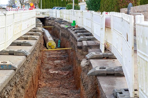 Construction site scene with district heating pipeline in a deep trench and white barriers