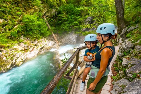 Mother carrying her son while observing stunning turquoise radovna river rapids flowing through
