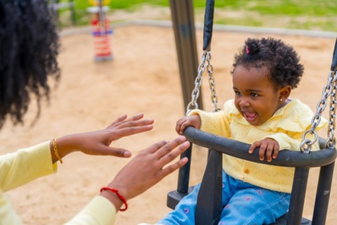 Cropped photo of an african girl and unrecognizable mother swinging in the park