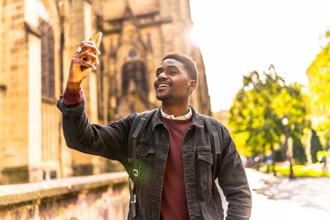 Happy african man walking along the city taking photos under the sunset