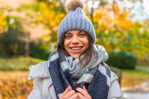 Portrait of a confident smiling woman with woolly hat and scarf in a park