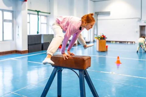 Redhead student practicing gymnastics on pommel horse, showing balance and coordination in school
