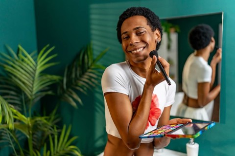 Portrait of a latin happy transgender person applying makeup in the bathroom at home