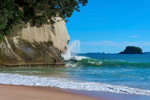 Breaking waves with spray in front of mighty cliffs by the sea, Cathedral Cove, Hahei, Coromandel