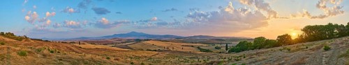 Typical Tuscan landscape in Val d'Orcia with hills, trees, fields, cypresses and farm road in