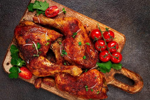 Grilled fried chicken legs, served with fresh cherry tomatoes, and herbs, on a wooden chopping
