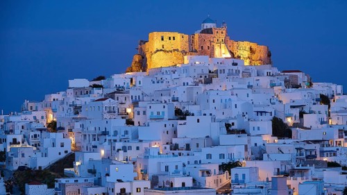Whitewashed buildings surround an illuminated fortress under a dark blue night sky, Querini Castle,