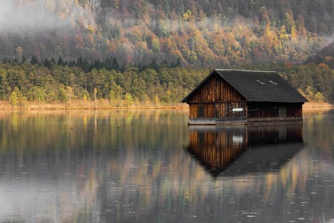 A boatshelter at lake Almsee. The forest in the background in full fall foliage and some fog above