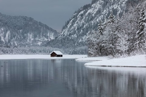 Snow covered boat shelter on Lake Almsee which is partly frozen and snow covered. Snow on the