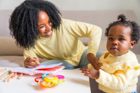 Adorable child and african mother drawing at home sitting on the sofa in the living room