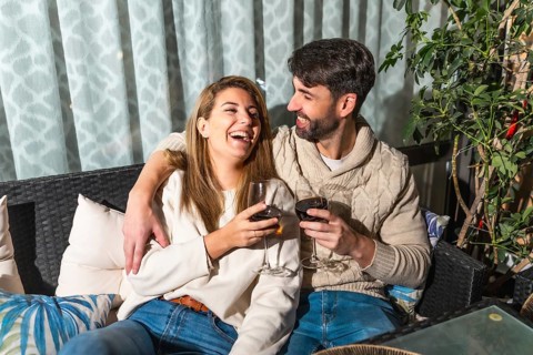 Cheerful couple enjoying a romantic evening, drinking wine and laughing together on a cozy terrace