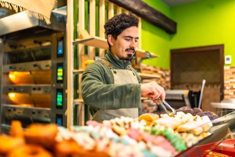 Latin young male baker arranging pastries on the counter of an artisan bakery shop