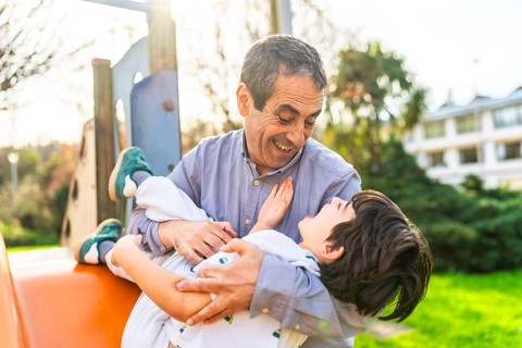 Grandfather holding his grandson and playing together at the playground, having a joyful and